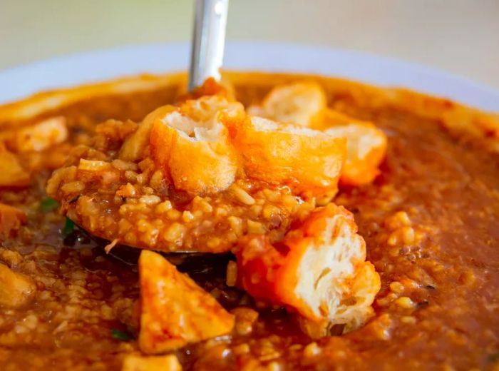 A spoon scoops up a mix of pork, yam, and prawns from a rich brown bowl of porridge.