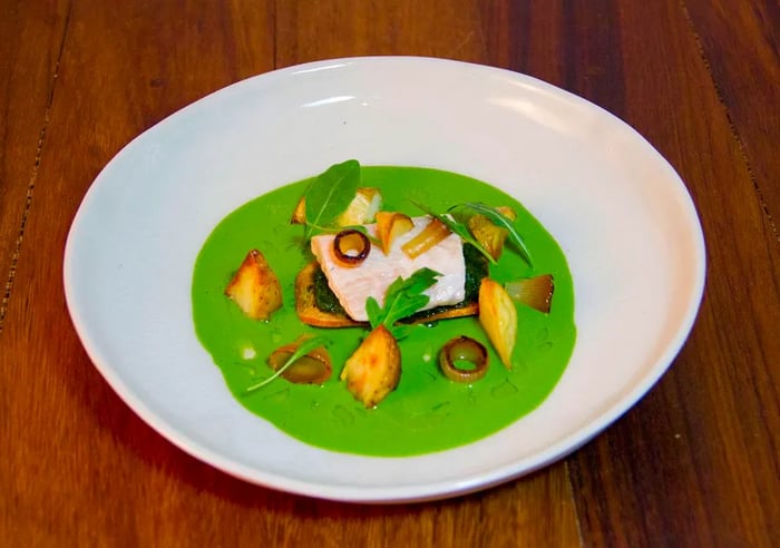 A beautifully cooked fish resting in a vibrant green sauce, accompanied by colorful vegetables