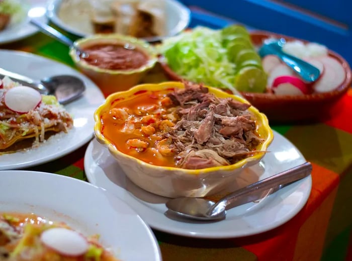 A beautifully arranged bowl of pozole, with generous portions of meat rising from the savory broth, accompanied by a variety of other dishes.