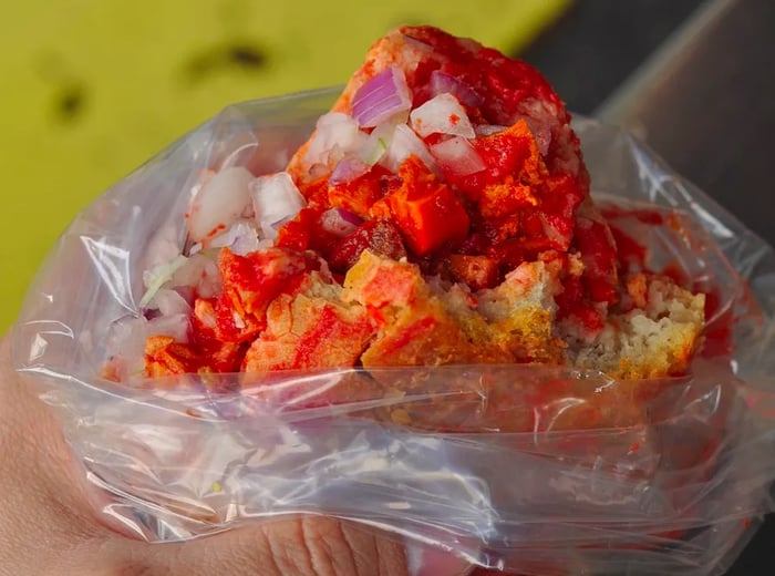 A partially eaten torta ahogada, nestled in a plastic bag with sauce pooled at the bottom, its fillings spilling over the edge