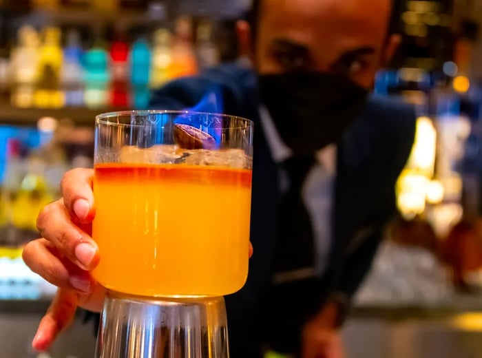 A bartender presents a vibrant two-tone cocktail, showcasing it for the camera.