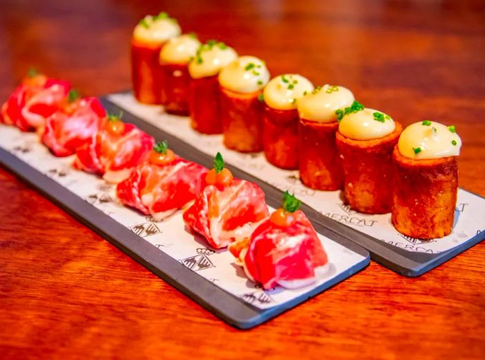 Delicious cream-filled pastries alongside pieces of dried meat arranged on slate boards atop a wooden table.