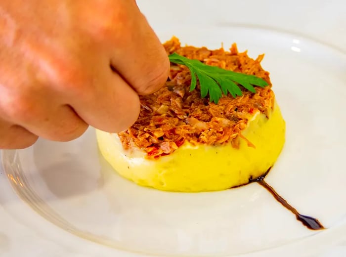 A chef carefully adds an herbal garnish to a plate of omelet topped with crispy delights.