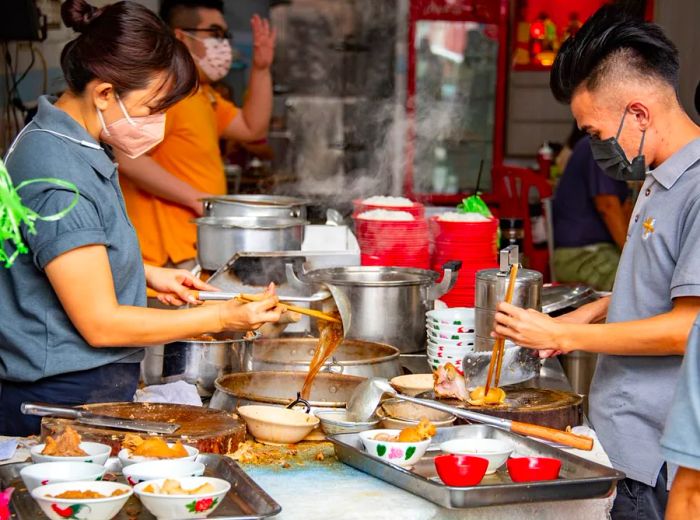 Chefs work diligently on either side of a kitchen counter, crafting bak kut teh.