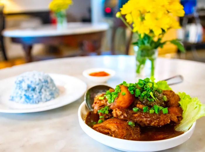 A serving of chicken stew alongside a plate of blue rice.