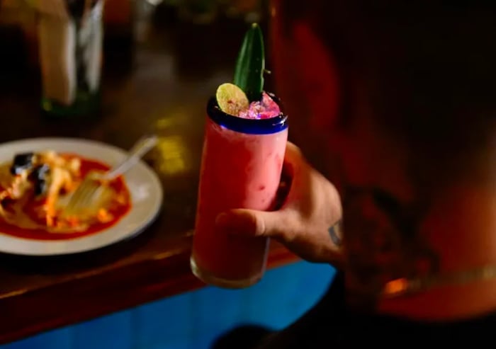 A drinker showcases a vibrant pink highball cocktail adorned with a pineapple leaf