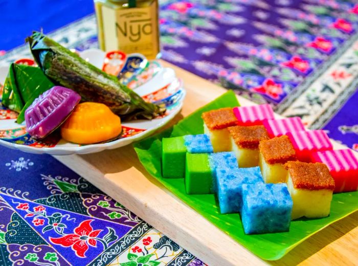 Vibrantly colored snacks in an array of shapes and sizes, some elegantly presented on a decorative plate, while others rest on leaves, all displayed on a stylish tablecloth.