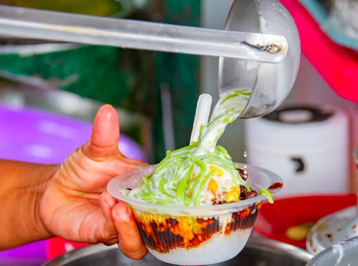 A person ladles chendol into a plastic cup.