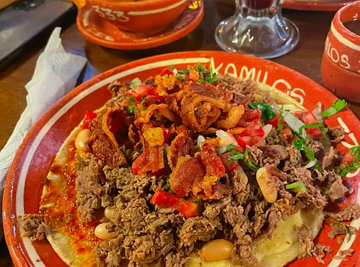 A generous serving of carne en su jugo on a beautifully decorated plate featuring the restaurant's name, accompanied by an array of other dishes on a rustic wooden table.