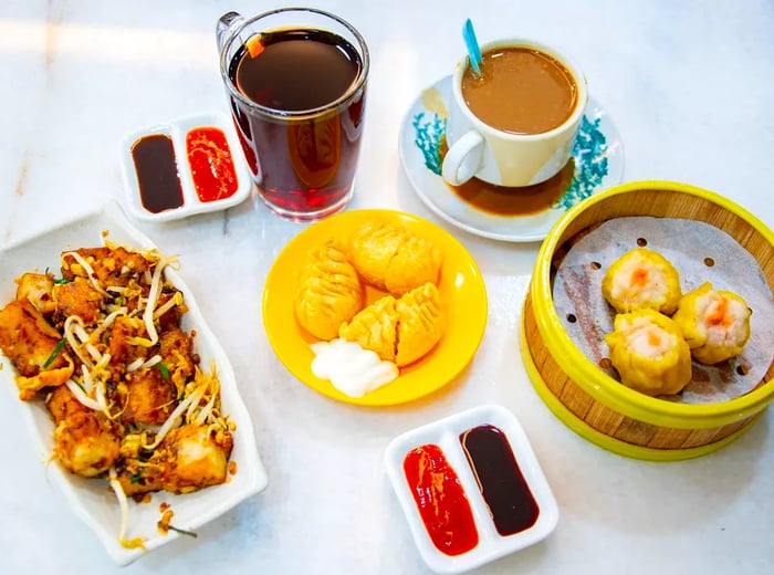 A selection of buns, dumplings, a stir-fried dish, dipping sauces, and beverages on a white background.