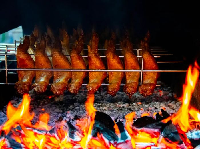 Chicken wings resting in a metal holder, grilling directly over a blazing charcoal fire.