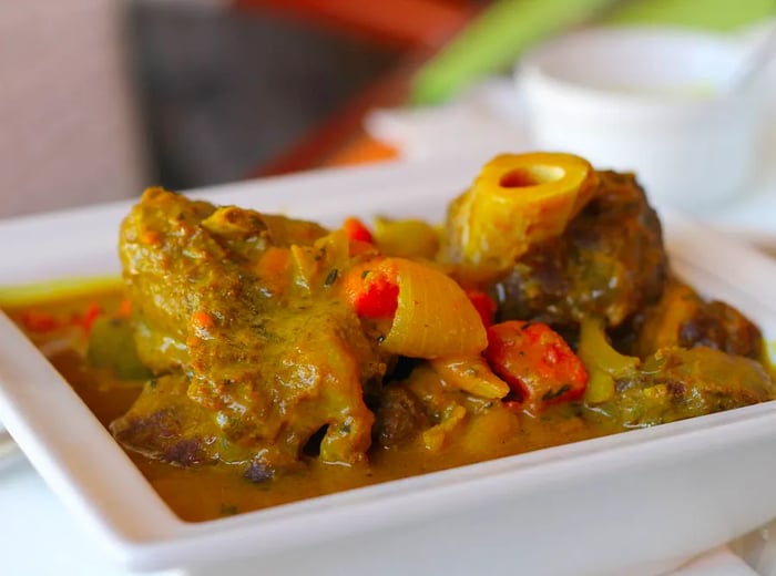 A bowl brimming with generous chunks of goat meat in a rich curry sauce accompanied by vegetables.