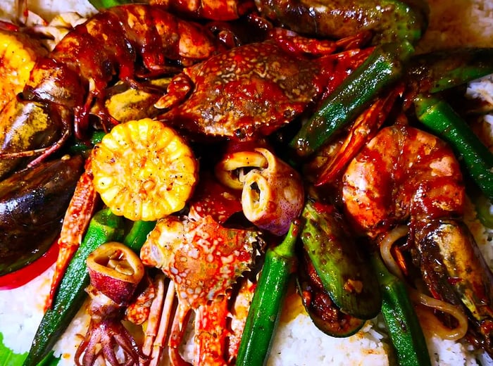 A vibrant assortment of seafood, corn cobs, and vegetables served atop a generous mound of rice on a large leaf