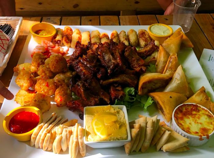 A generous platter featuring grilled meats, fried pastries, and an array of dipping sauces.