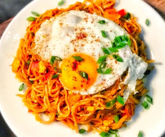 Aerial view of a large fried egg sitting atop a bed of noodles sprinkled with herbs.