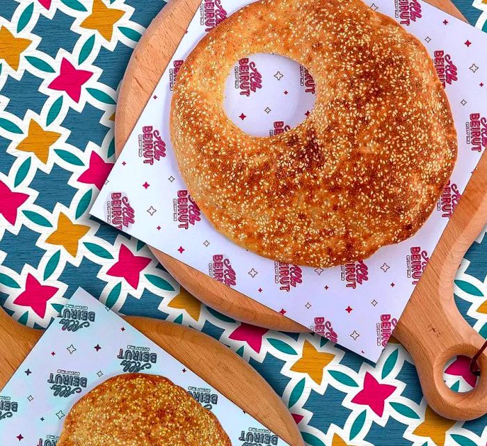 A kaak sprinkled with za’atar resting on branded wax paper atop a vibrant patterned tablecloth.