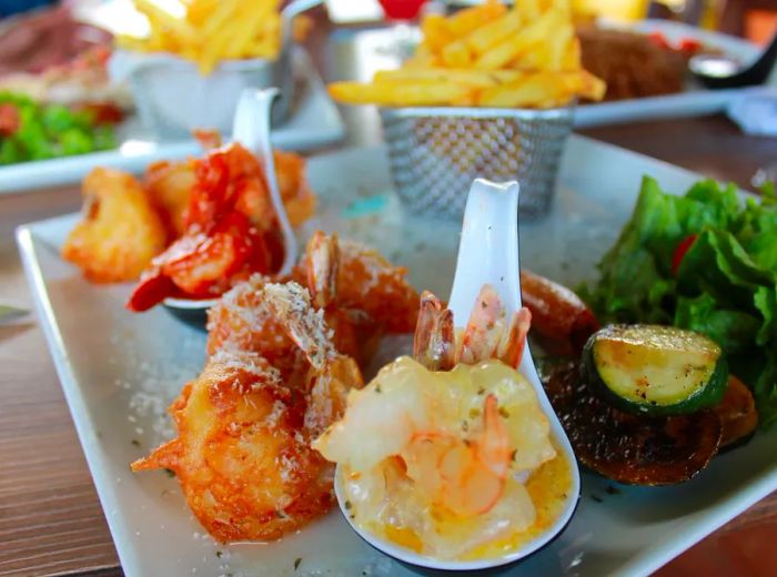 An assortment of shrimp dishes arranged on a bed of ice, accompanied by a basket of French fries in the background.