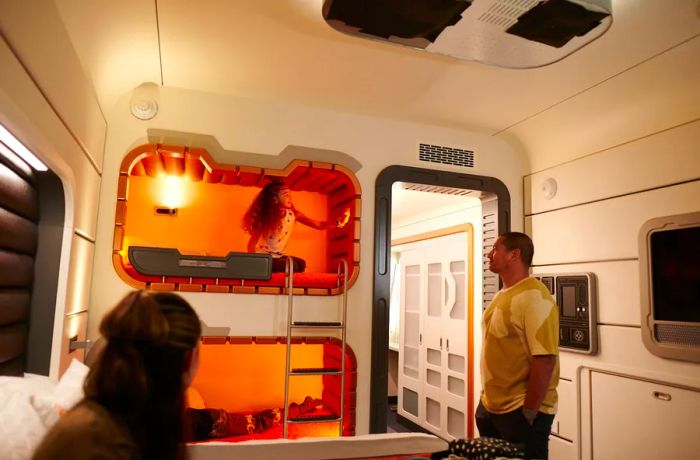 A young girl enjoys herself in a vibrant orange futuristic bunk bed, while her parents watch with delight.