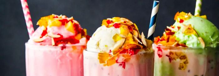 Three soda fountain glasses brimming with vibrant falooda, topped with an assortment of delights