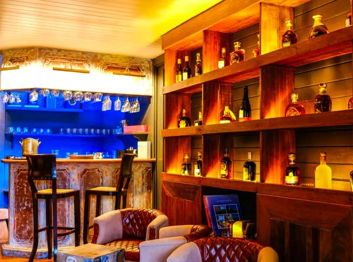 The interior of a bar featuring illuminated wooden shelves stocked with rum bottles, a blue-lit counter, and leather seating.