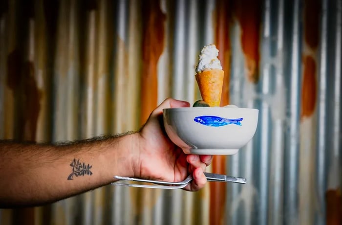 A server presents a bowl featuring a fish design, with a ceviche cone topped by a layer of foam protruding from the top