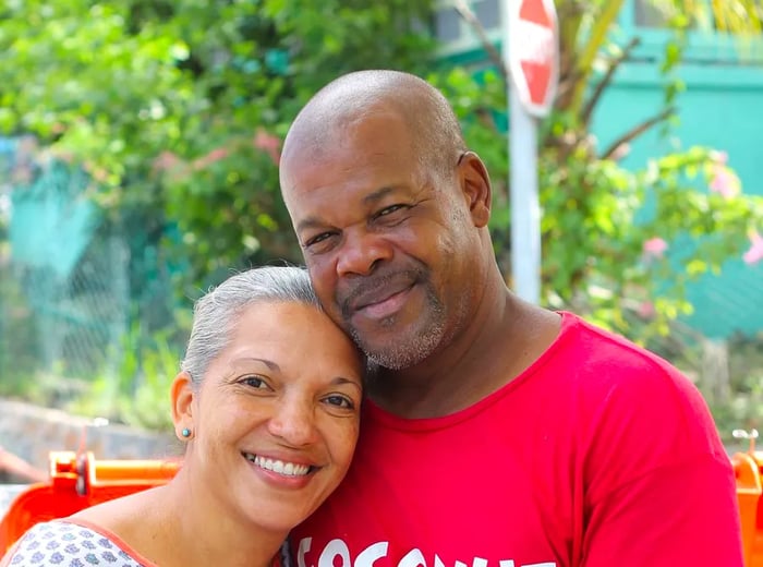 A couple stands outside, joyfully holding a freshly cut coconut.