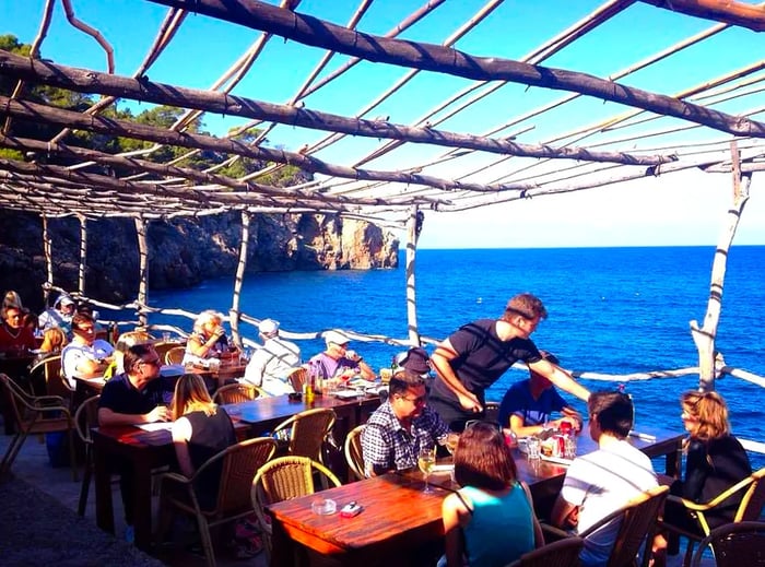 Diners enjoying their meals at tables on a picturesque jetty by the water.