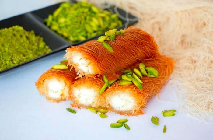 Rolls of knafeh arranged neatly on a white surface, surrounded by various ingredients in the background