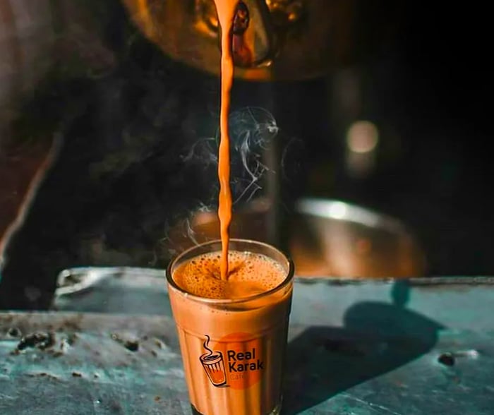 An antique copper kettle gracefully pours chai tea into a branded glass.