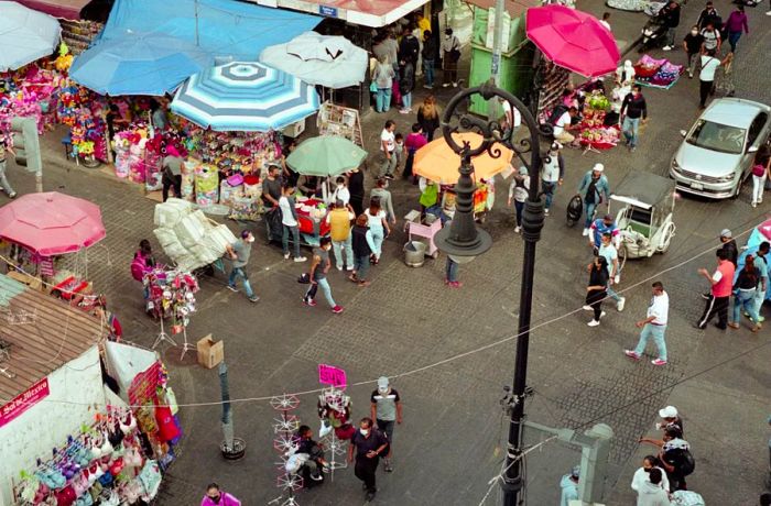 A collection of four photos showcases a variety of pastries, a man sitting at a table, a club sandwich with French fries on a plain white plate, and an aerial view of a bustling street corner.