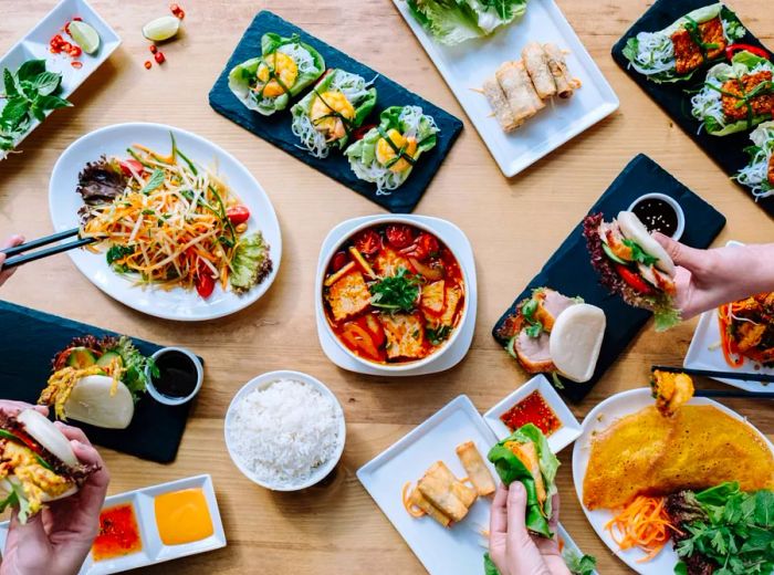 Aerial view of a wooden table laden with various dishes, including sandwiches, buns, and lettuce wraps.