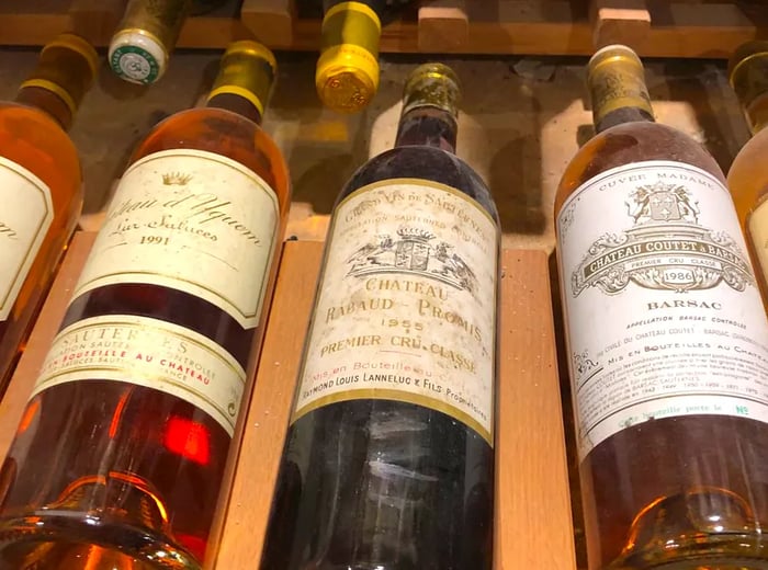 Three dusty bottles of Sauternes resting on a wine rack.