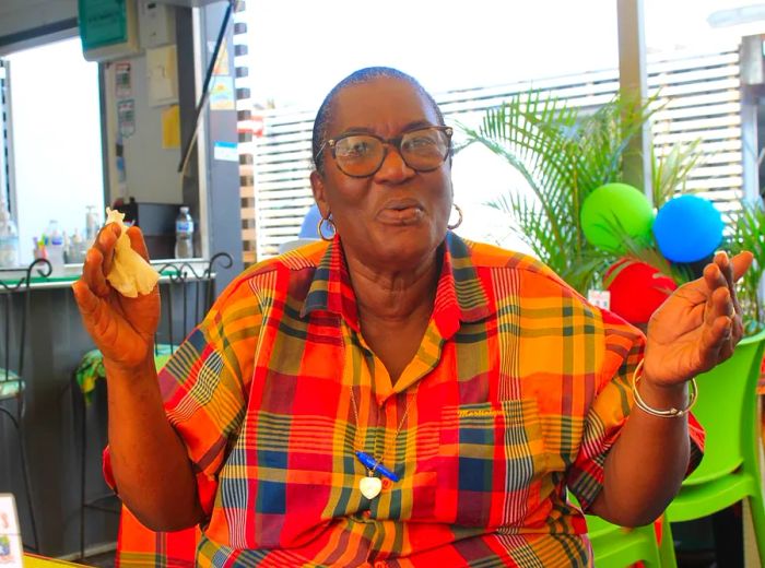 A woman seated at a restaurant expresses warmth with open arms and a welcoming smile.