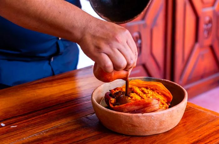 A sweet potato in a clay bowl, generously topped with rich brown mole.