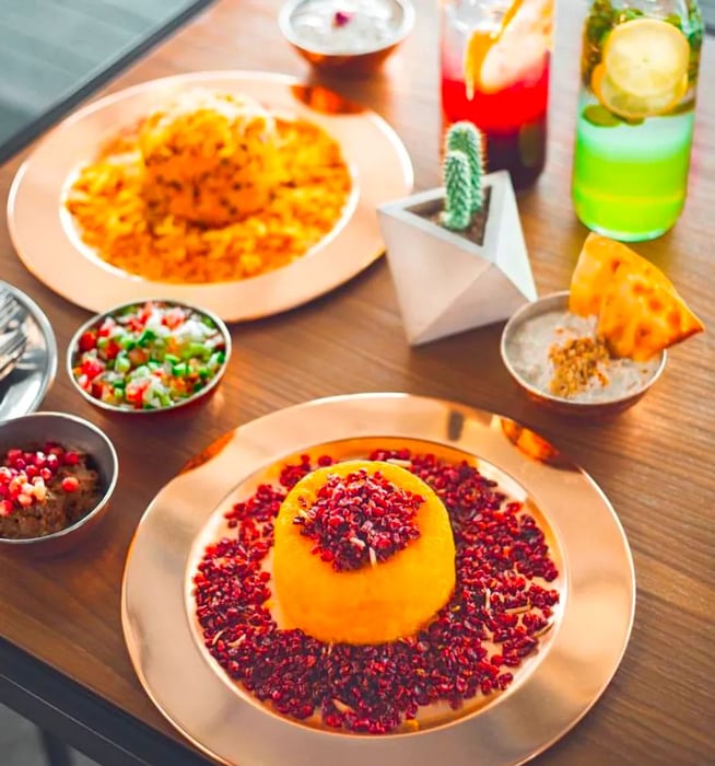 A heap of crispy rice adorned with barberries, accompanied by drinks and side salads