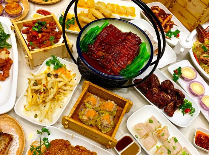 A table brimming with dim sum delicacies presented in baskets and platters, featuring dumplings, roasted meats, rice rolls, egg tarts, and buns.