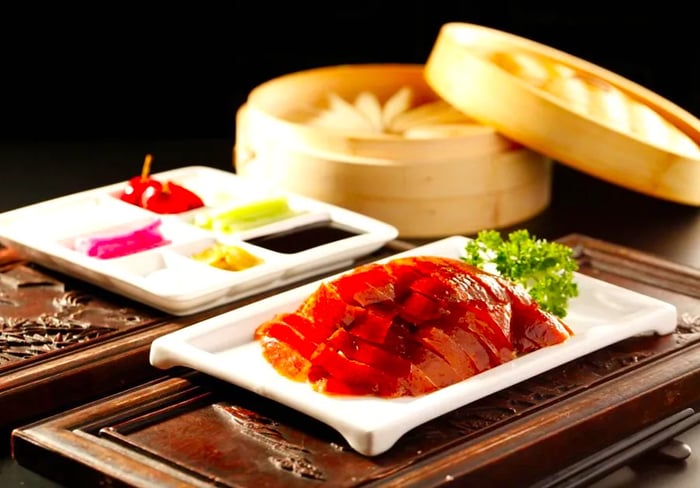 Plates of succulent roast duck accompanied by a variety of dipping sauces and a large steamer basket