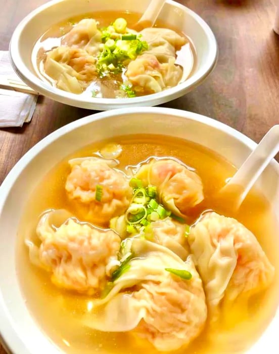 A bowl filled with textured shrimp wontons garnished with chopped scallions swimming in broth