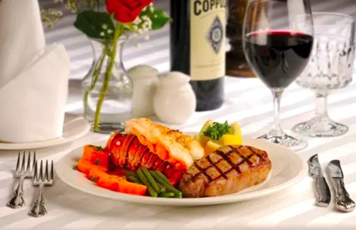 A beautifully presented plate featuring thick-cut grilled steak alongside lobster, elegantly arranged on a white tablecloth with fine dining settings