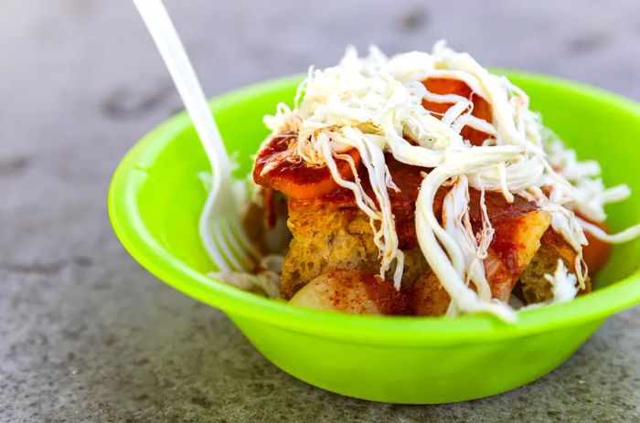 A green bowl filled with bread cubes drizzled with sauces.