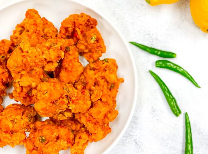 An aerial view of a plate heaped with chicken pakoras, accompanied by scattered chiles