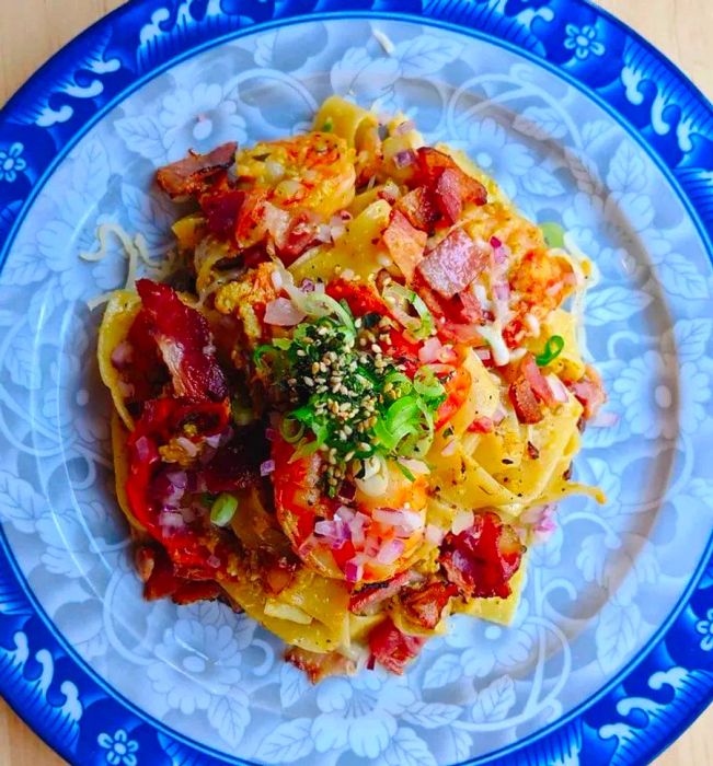 A plate of pappardelle noodles topped with crab, shrimp, bacon, roe, and a sprinkle of cheese