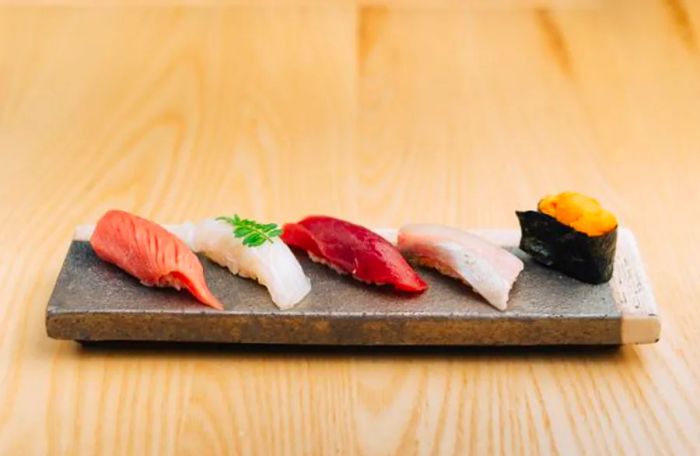 Five pieces of nigiri, featuring rich, vibrant slices of fish, presented on a wooden plank