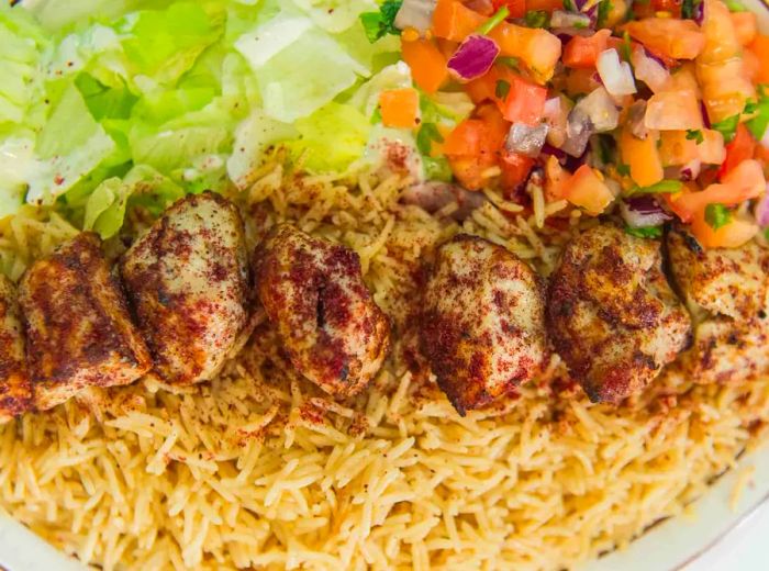 Skewered grilled kebabs served over a bed of rice with fresh salads