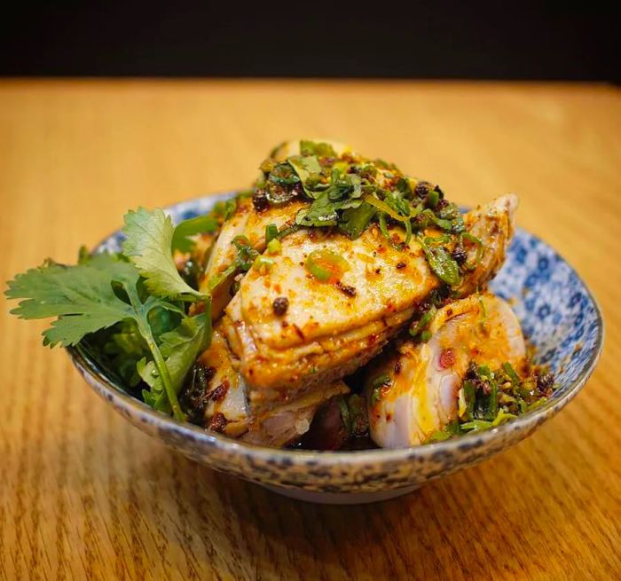 Slices of chicken artfully arranged in a decorative ceramic bowl, sprinkled with ground spices and herbs