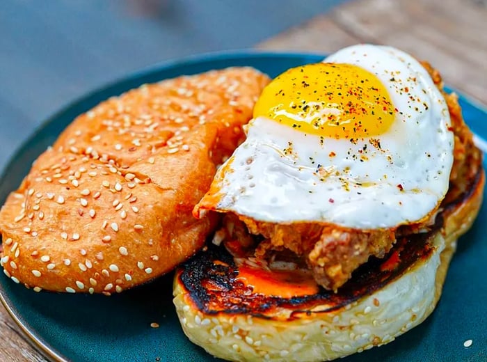 A fried chicken sandwich served on a long sesame seed bun, topped with a fried egg