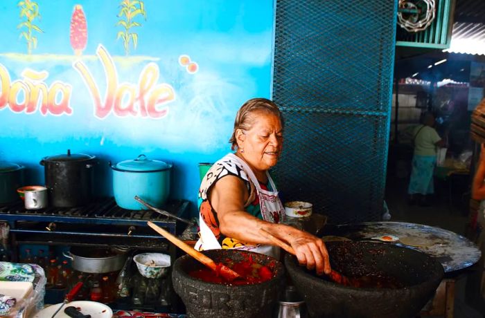 Doña Vale stands before a hot comal, reaching for one of her freshly made salsas crafted daily in her molcajetes.