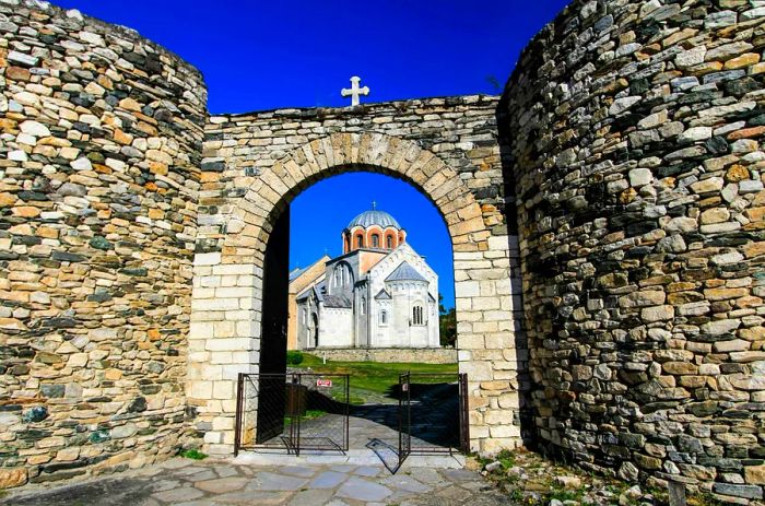 A domed monastery framed by a stone archway topped with a cross