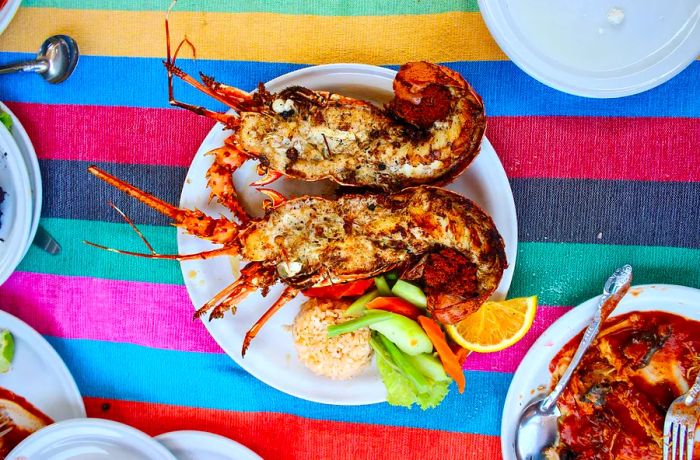 A halved roasted lobster served on a plate alongside rice and colorful garnishes on a vibrant tablecloth.