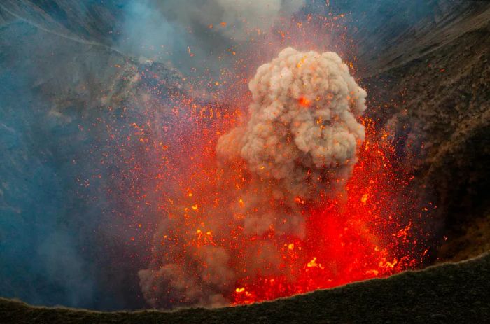 A massive plume of smoke, surrounded by a burst of magma, billows from the crater of Mt Yasur.